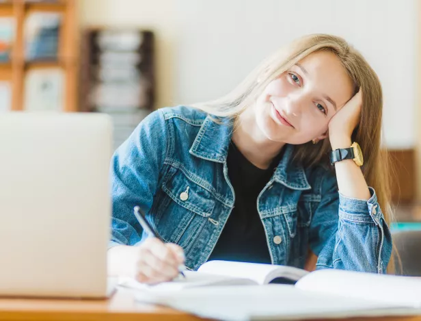 smiling-teen-making-notes-near-laptop